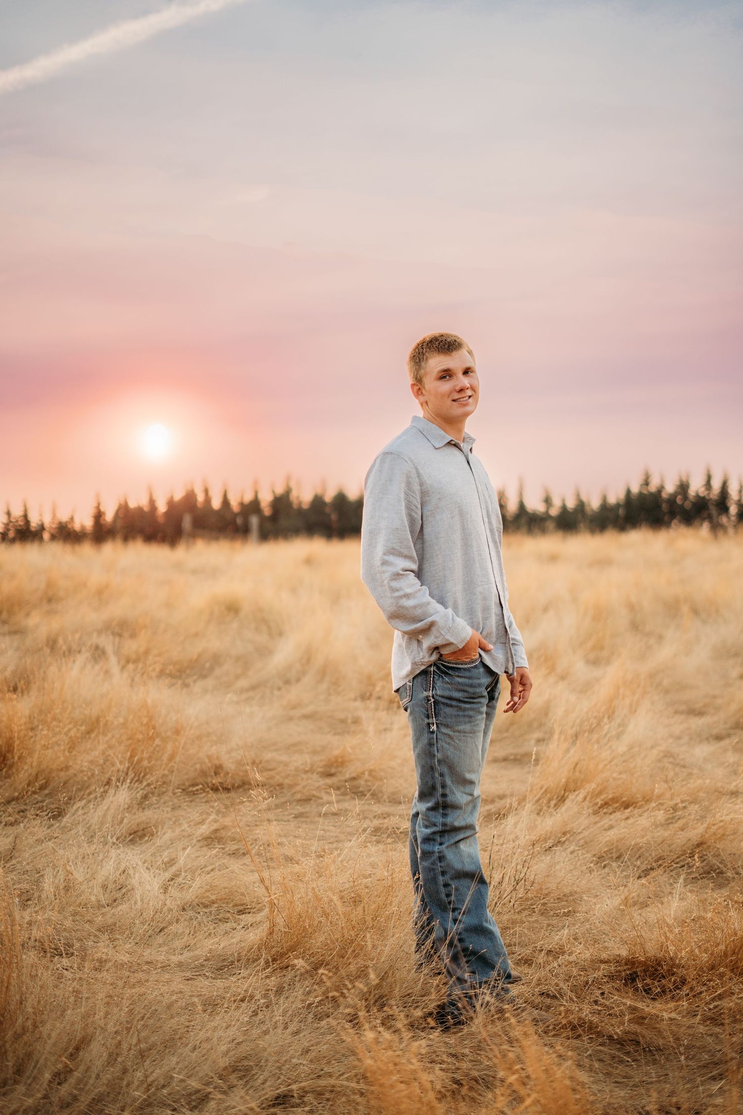 Senior boy standing in tall grass during sunset
