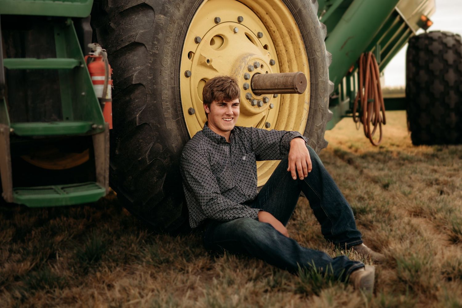 Senior boy sitting beside farm equipment with relaxed smile