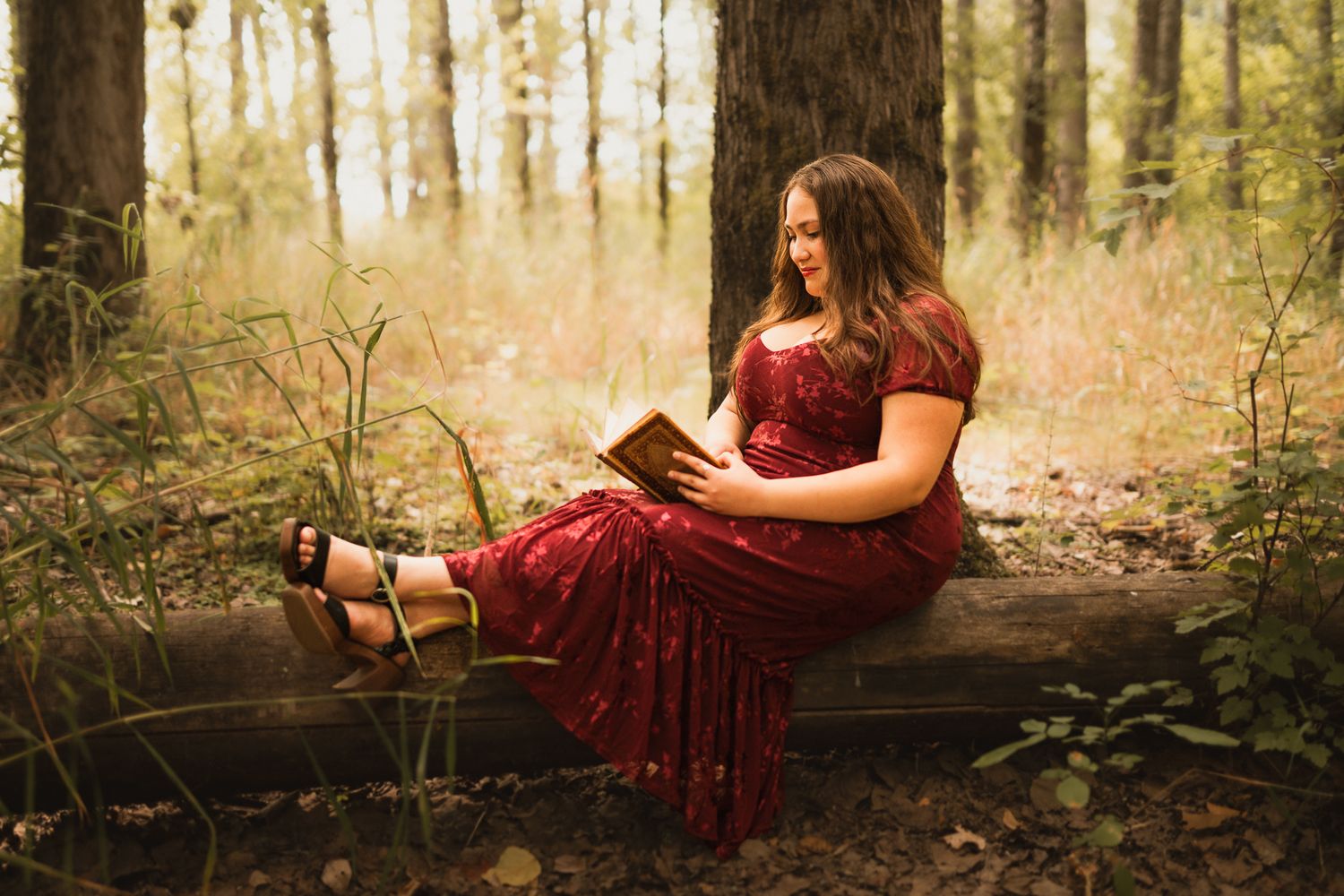 Senior girl sitting in woods reading a book with flowing dress
