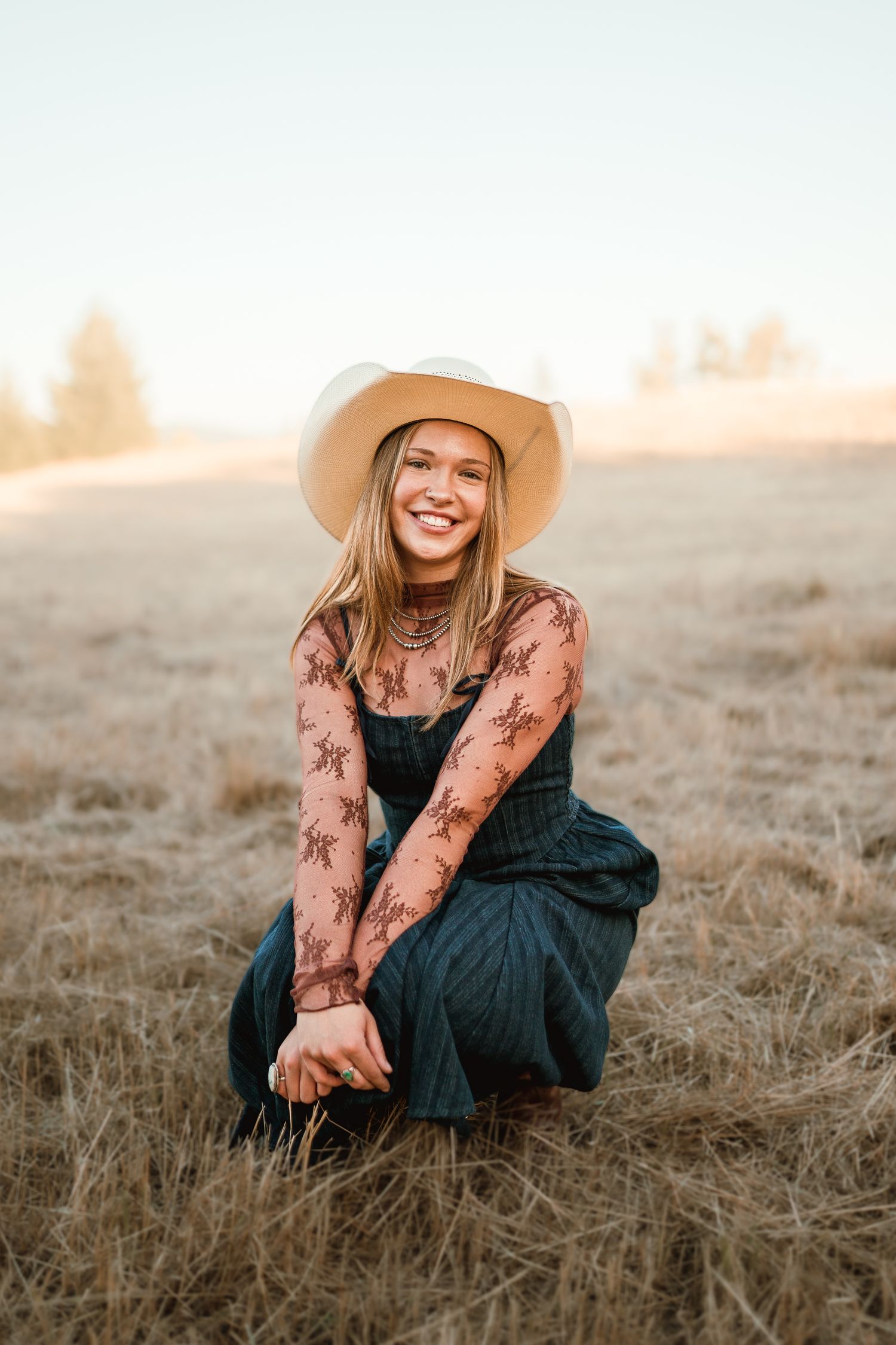 Senior girl crouched down smiling confidently at golden hour