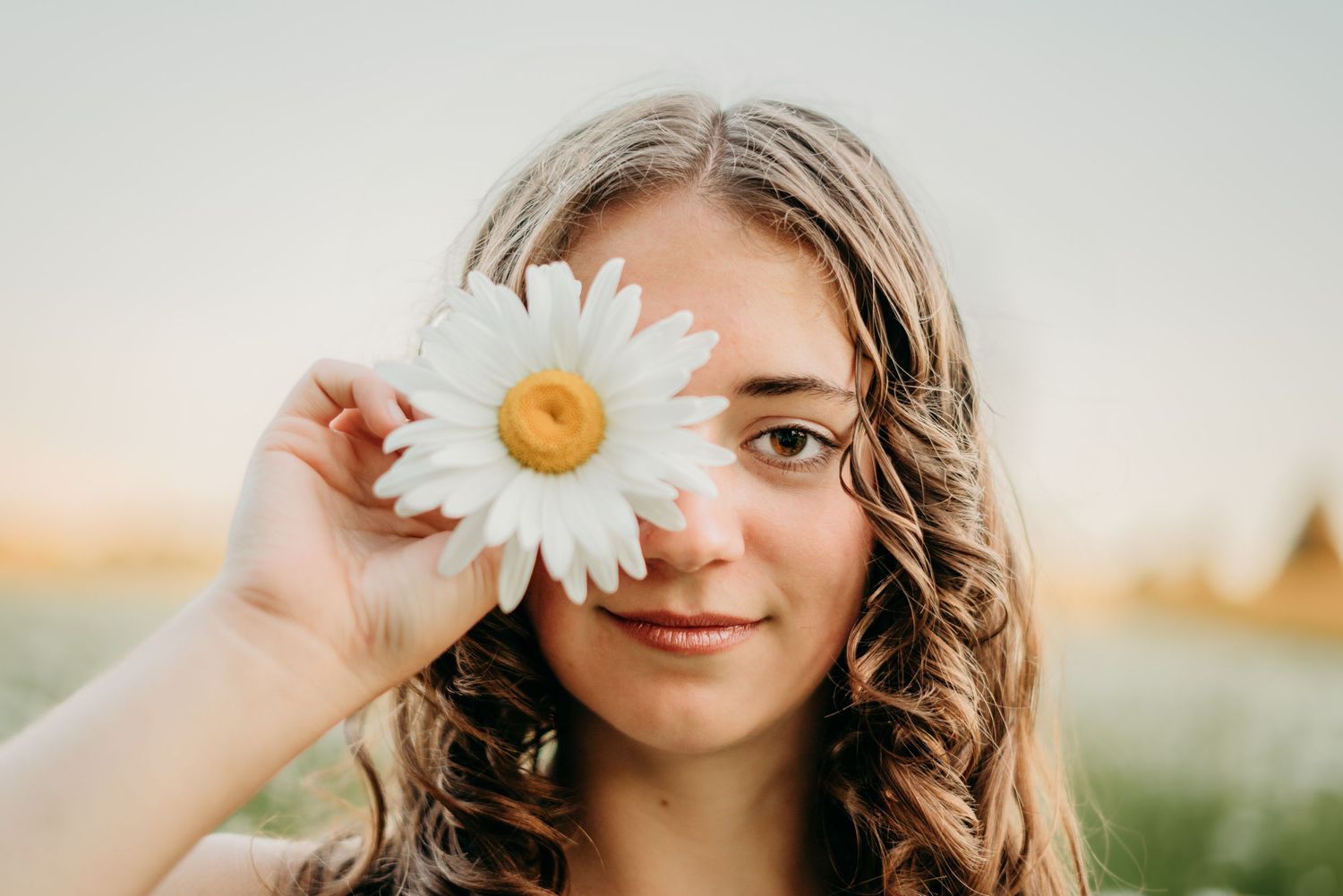 Close-up senior girl holding a daisy in front of her eye