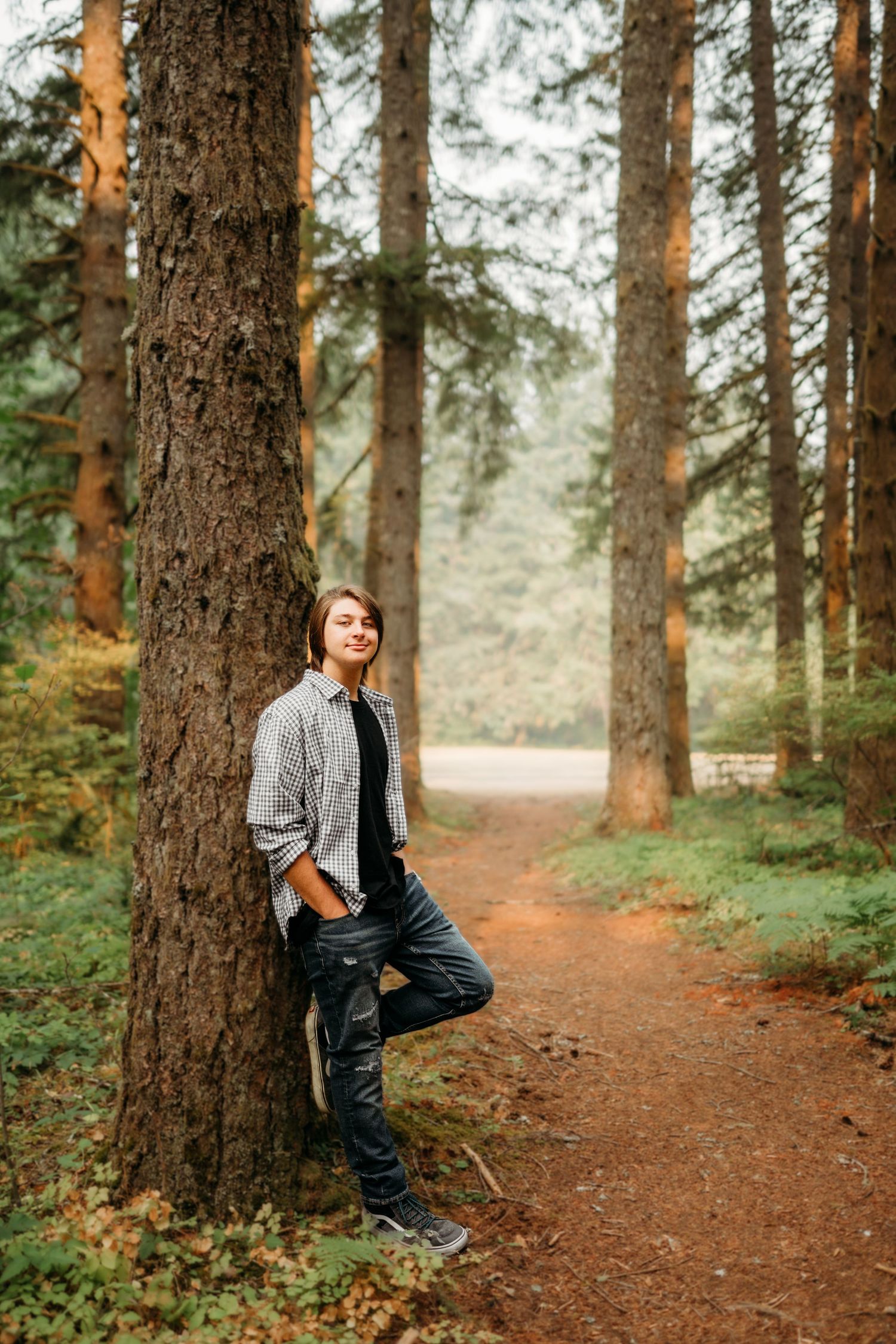 Senior boy leaning against a tree in a forest trail.