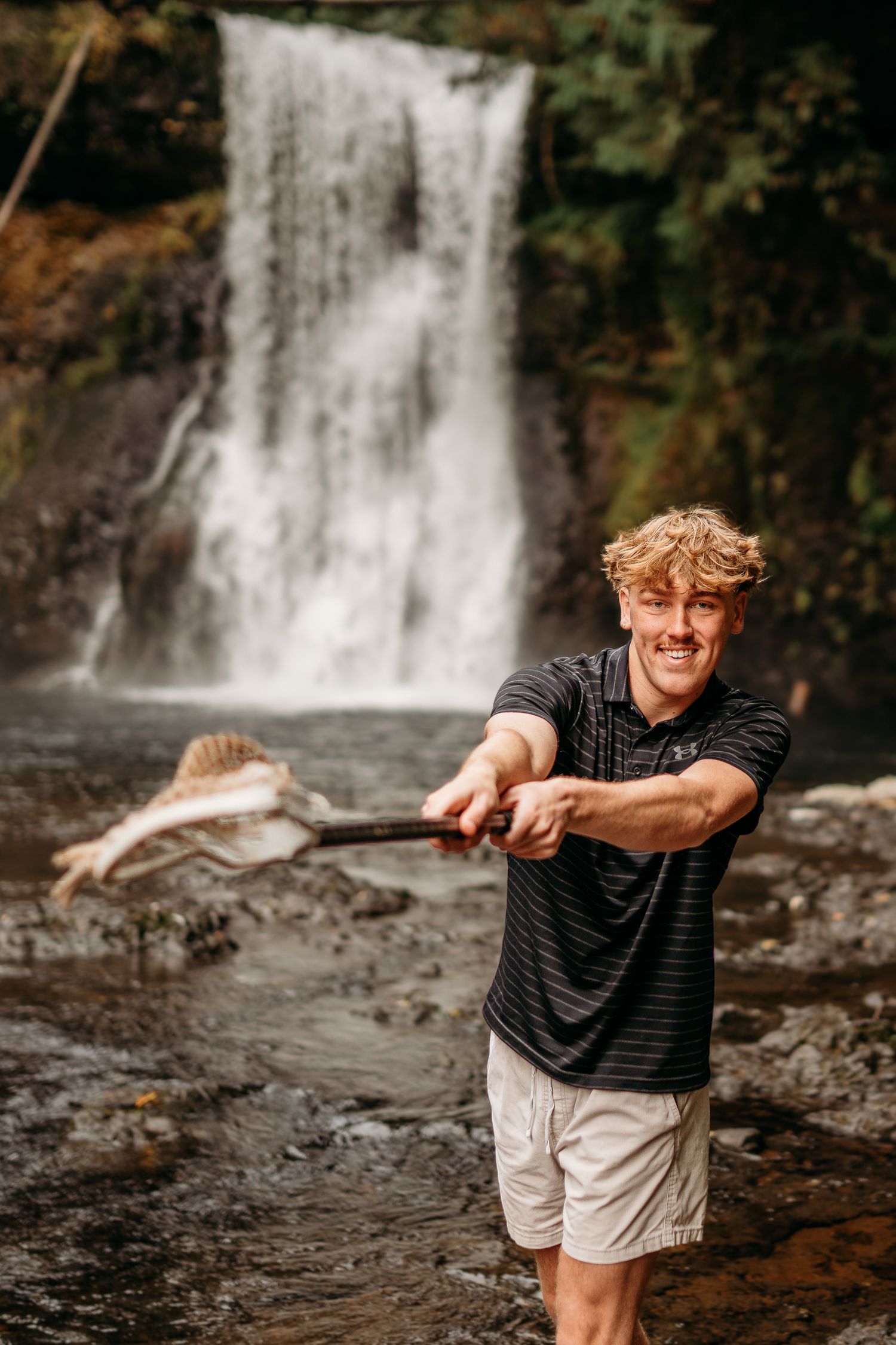 Senior boy standing near a waterfall during an outdoor portrait session at Silverfalls State Park in Oregon.