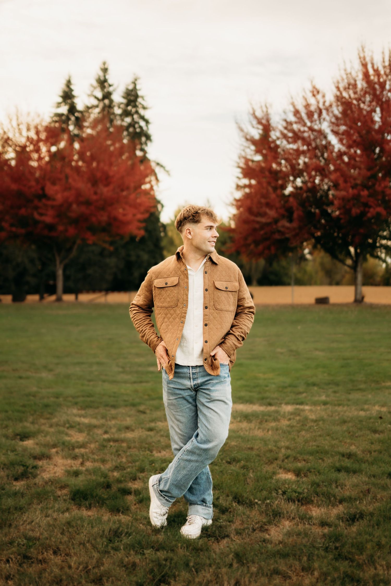 Senior boy standing in a park with autumn trees in the background