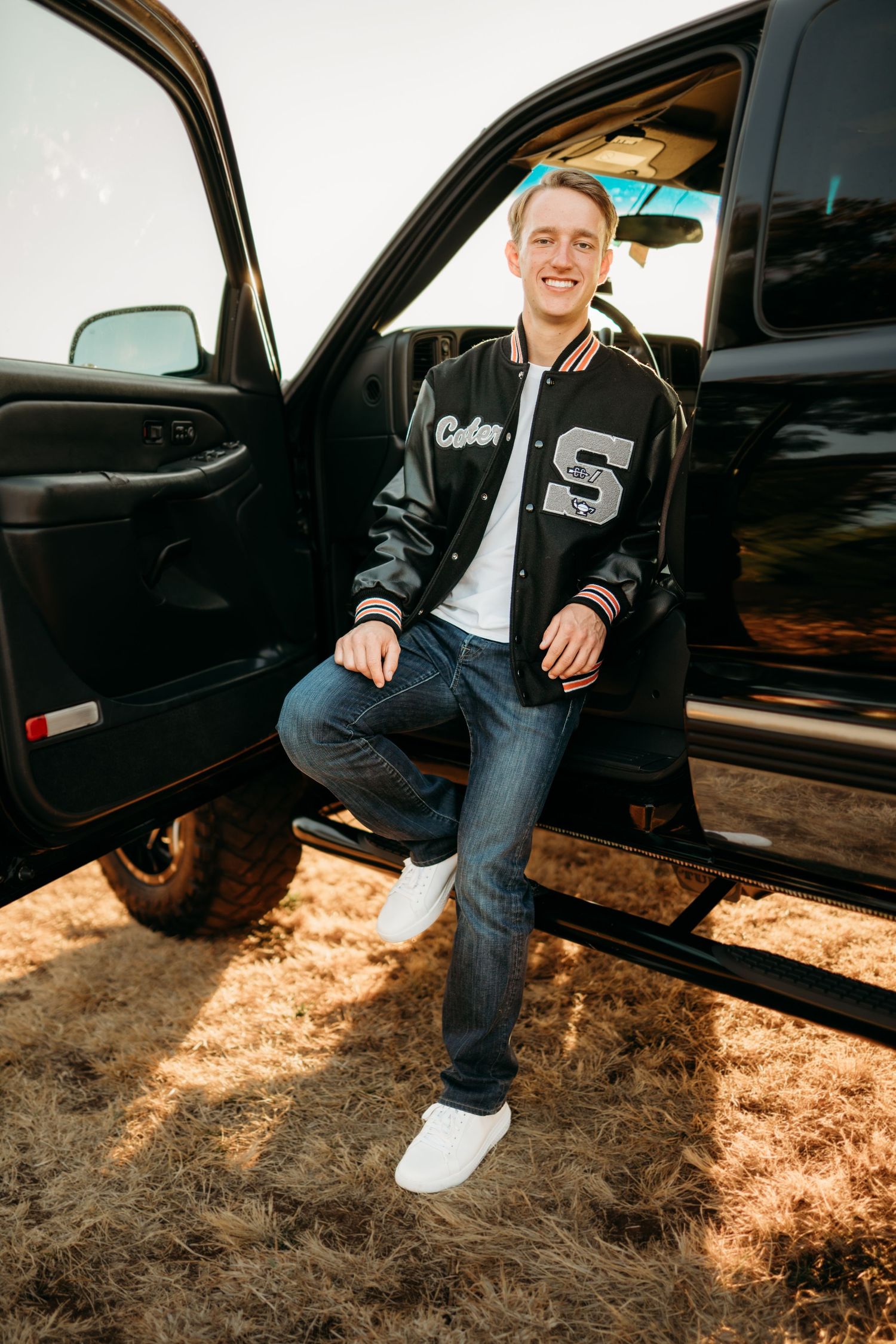 Senior boy sitting in a truck doorway with relaxed posture