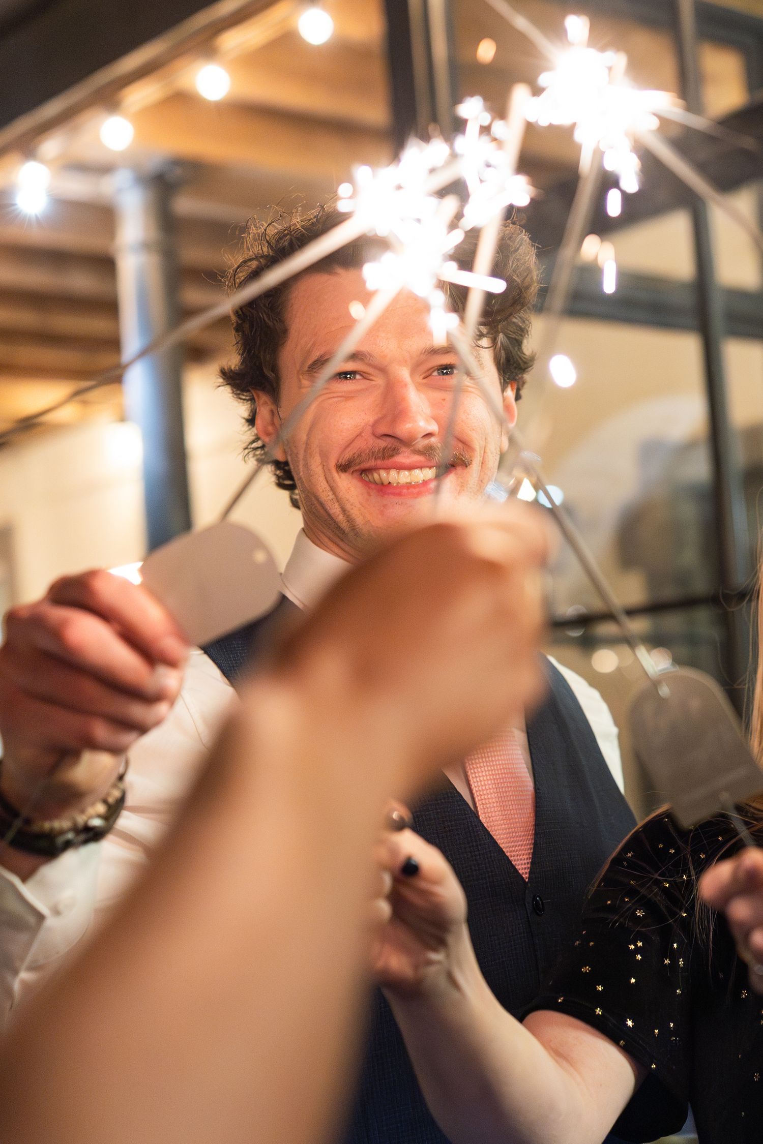 Smiling wedding guest holds sparklers during festive outdoor evening wedding reception celebration.
