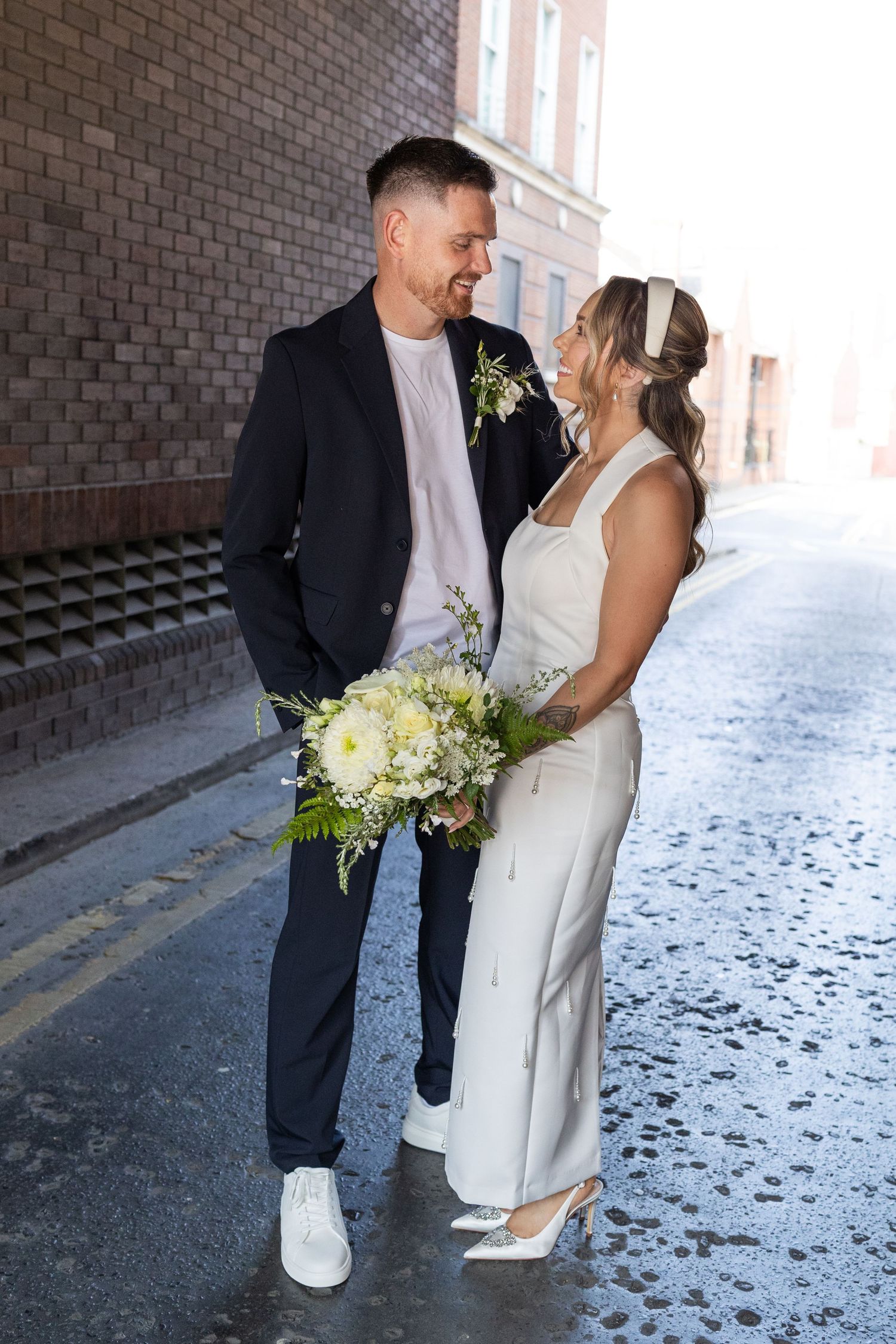 Smiling bride and groom in white and navy wedding attire sharing a romantic moment on a city street.