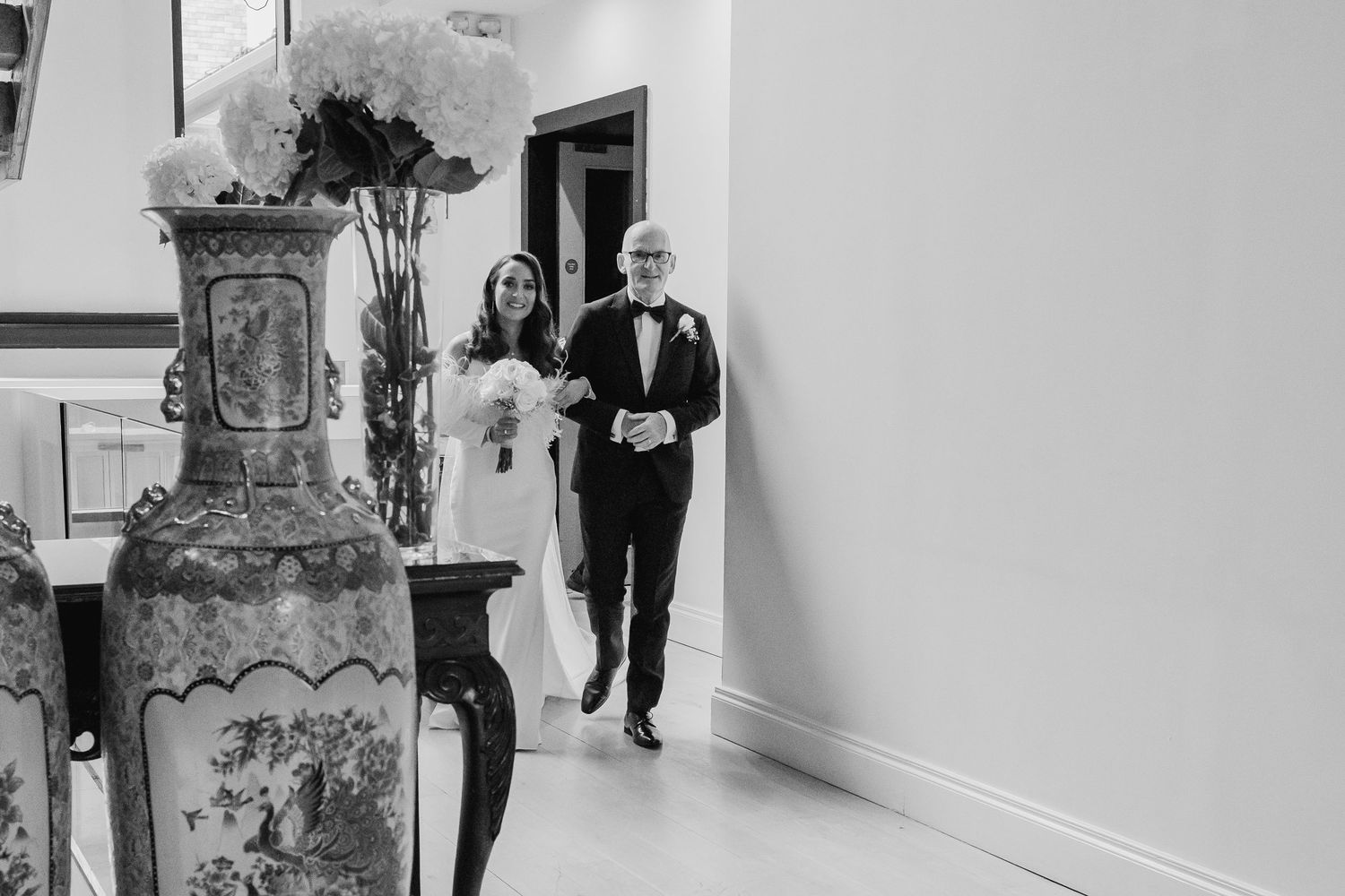 Wedding party members walking through a modern venue hallway in black and white.