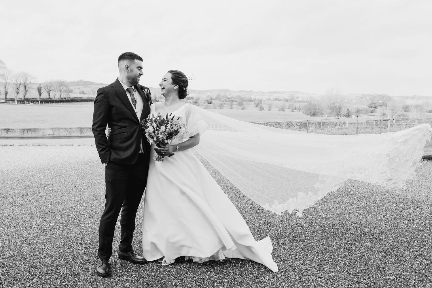 A couple walks through an outdoor field on their wedding day in black and white.