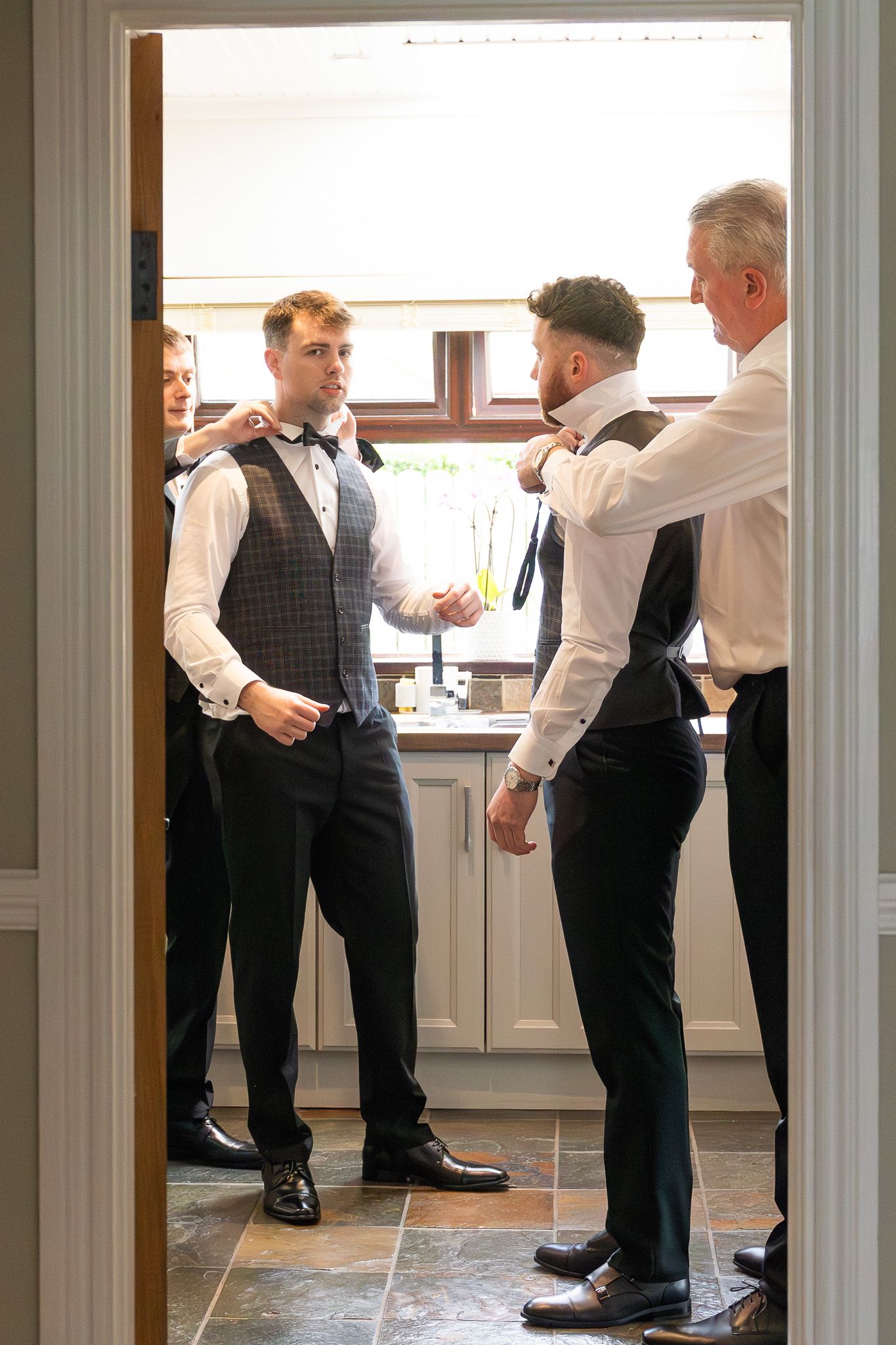 Group of people in formal attire gathered in a bright kitchen doorway ahead of Dublin city wedding.