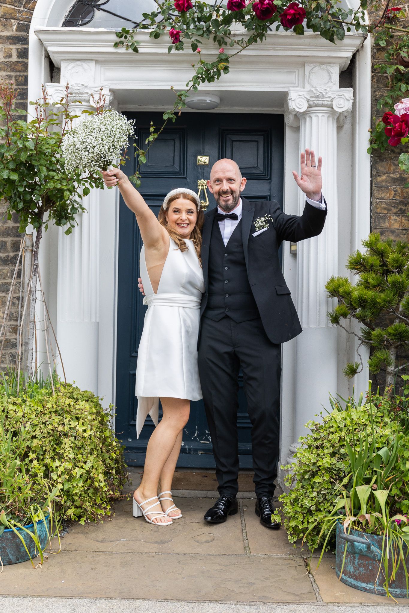 Newlyweds pose playfully in front of Dublins 25 Fitzwilliam place with white columns and flowering vines.