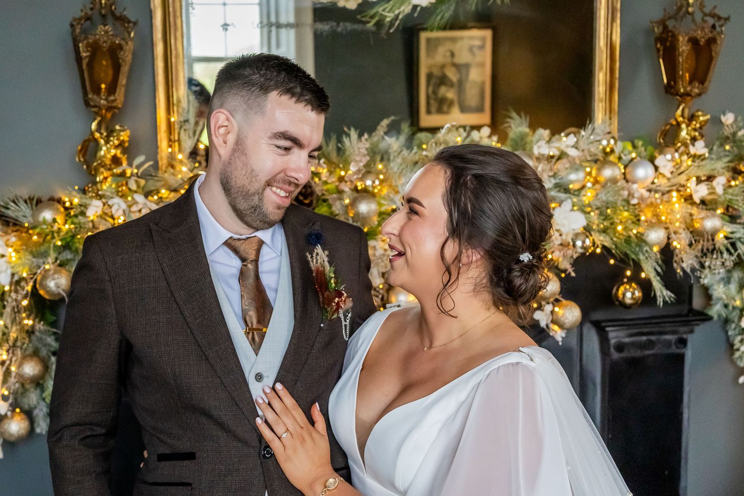 Bride and groom share a romantic moment by a gold Christmas floral display at their winter wedding.