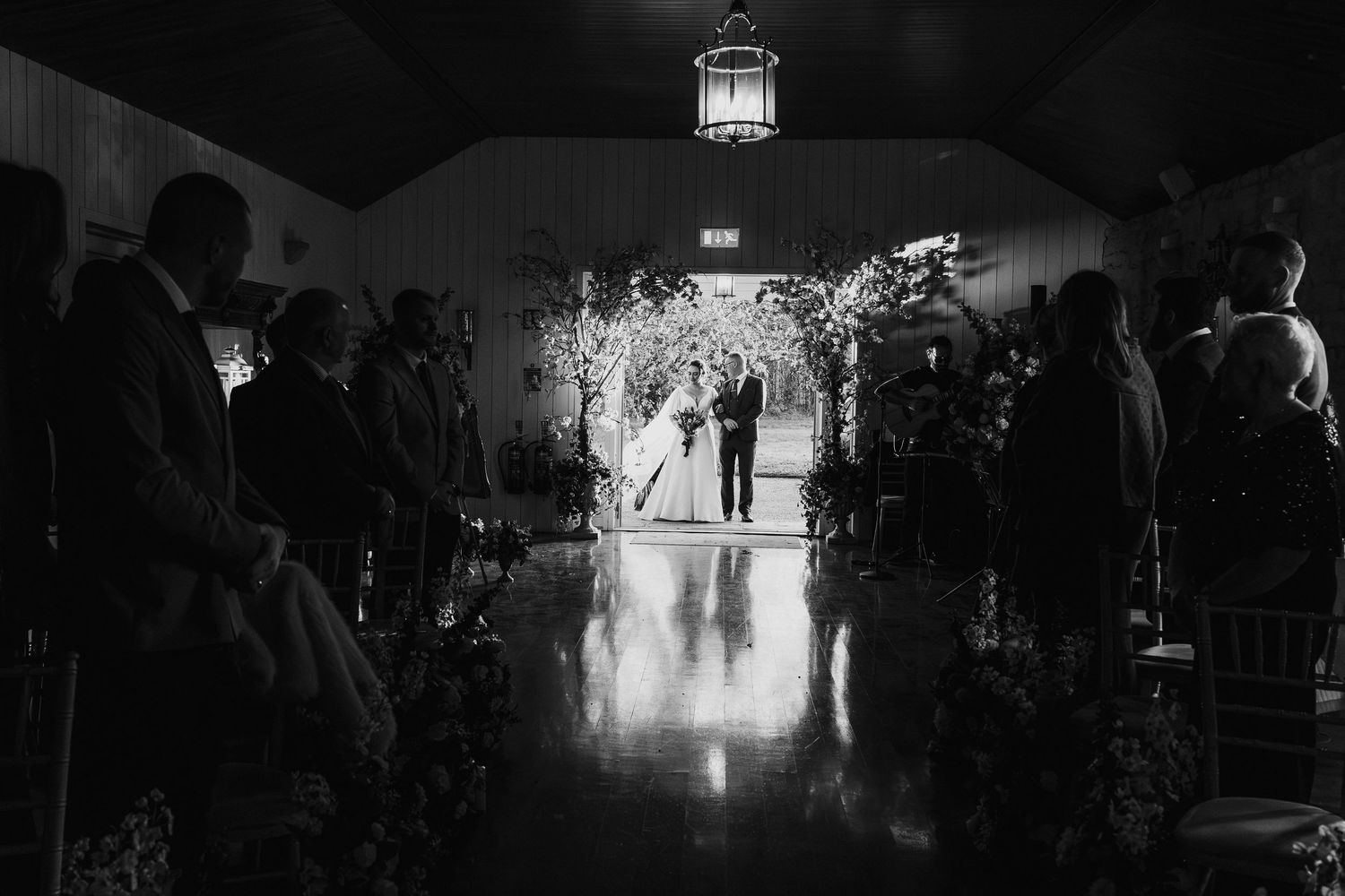 Black and white silhouette of bride and groom at floral arch during romantic indoor wedding ceremony.