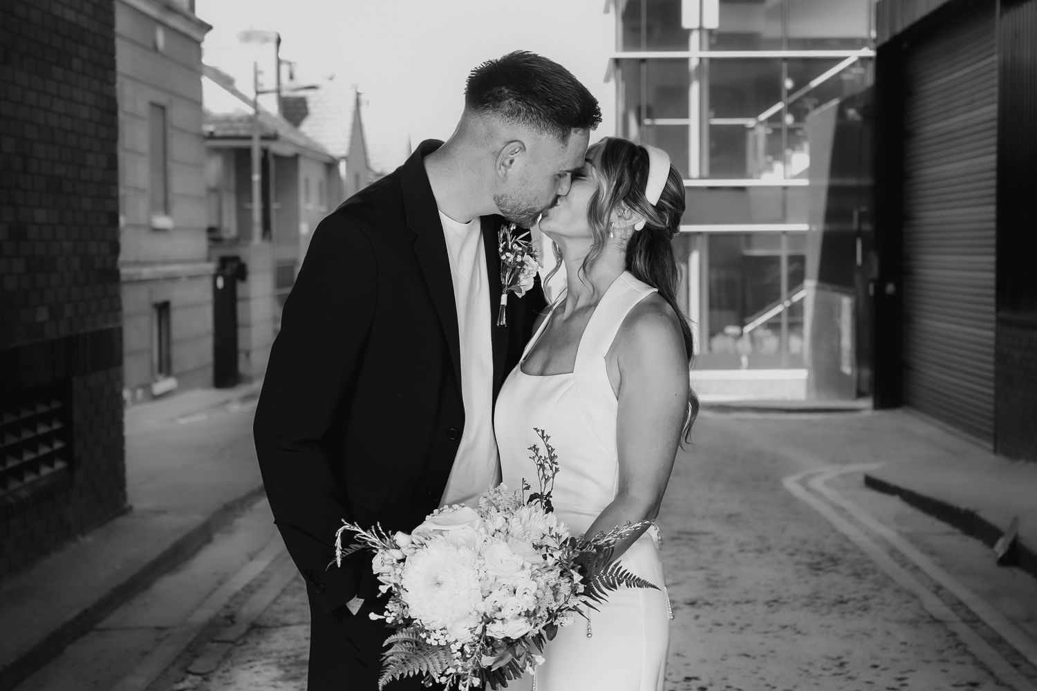 Bride and groom share a romantic kiss outdoors in a black and white wedding portrait.