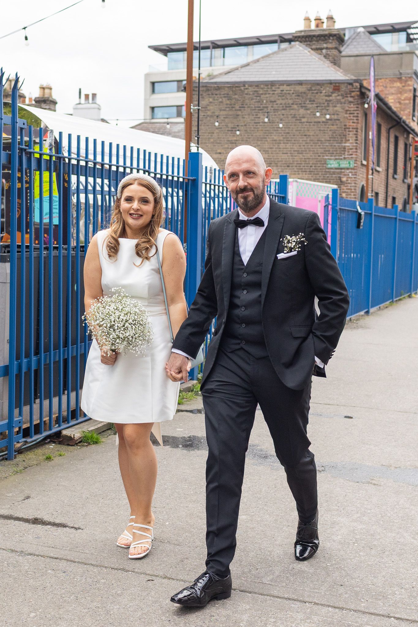 Dublin wedding couple walking along blue fence on Dublin city street.