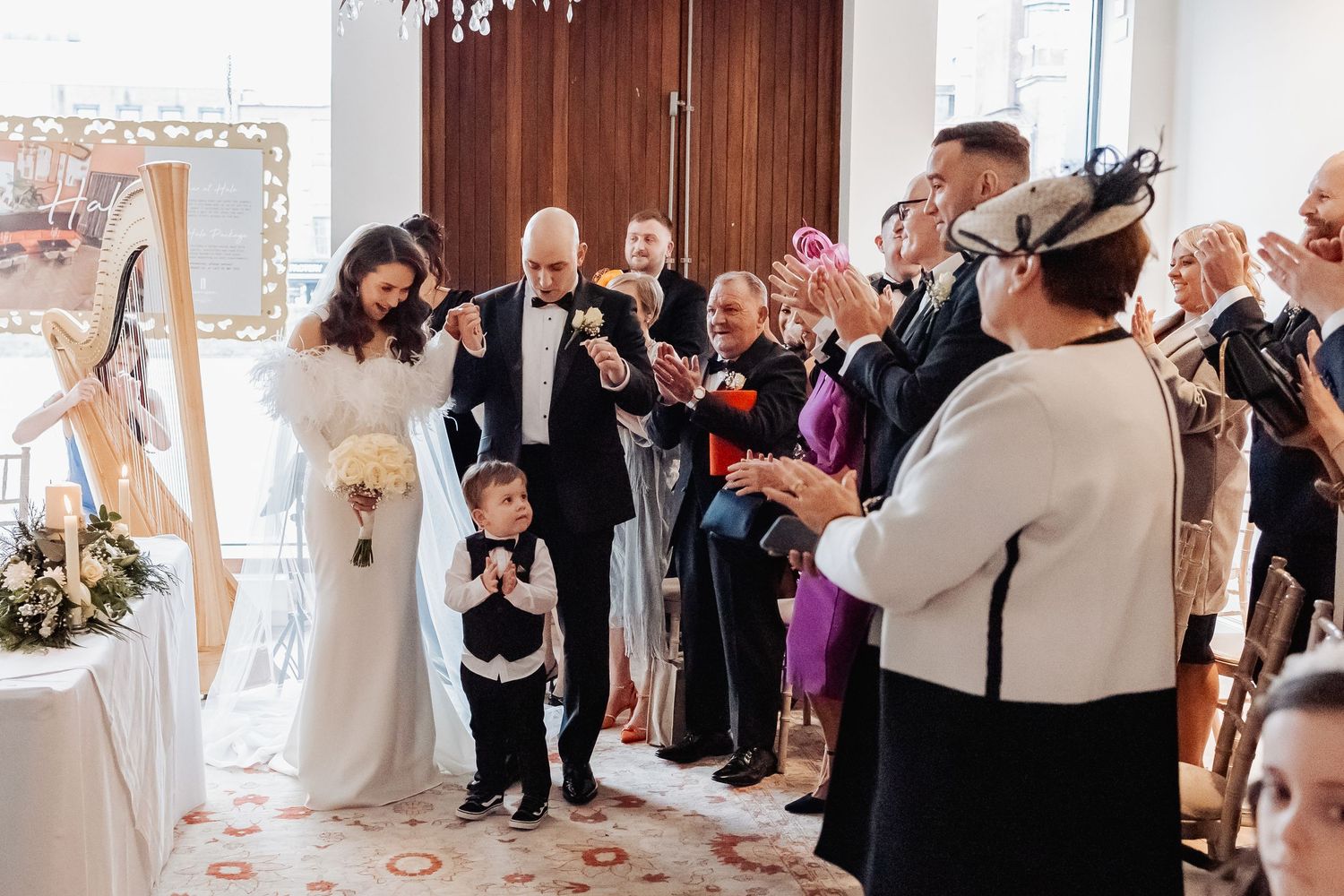 Wedding guests gather in an elegant venue with white decor and natural lighting.