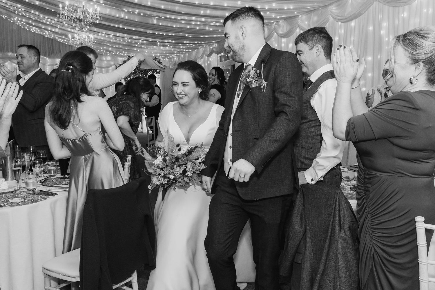 Wedding reception dance floor filled with guests celebrating under decorative lighting.