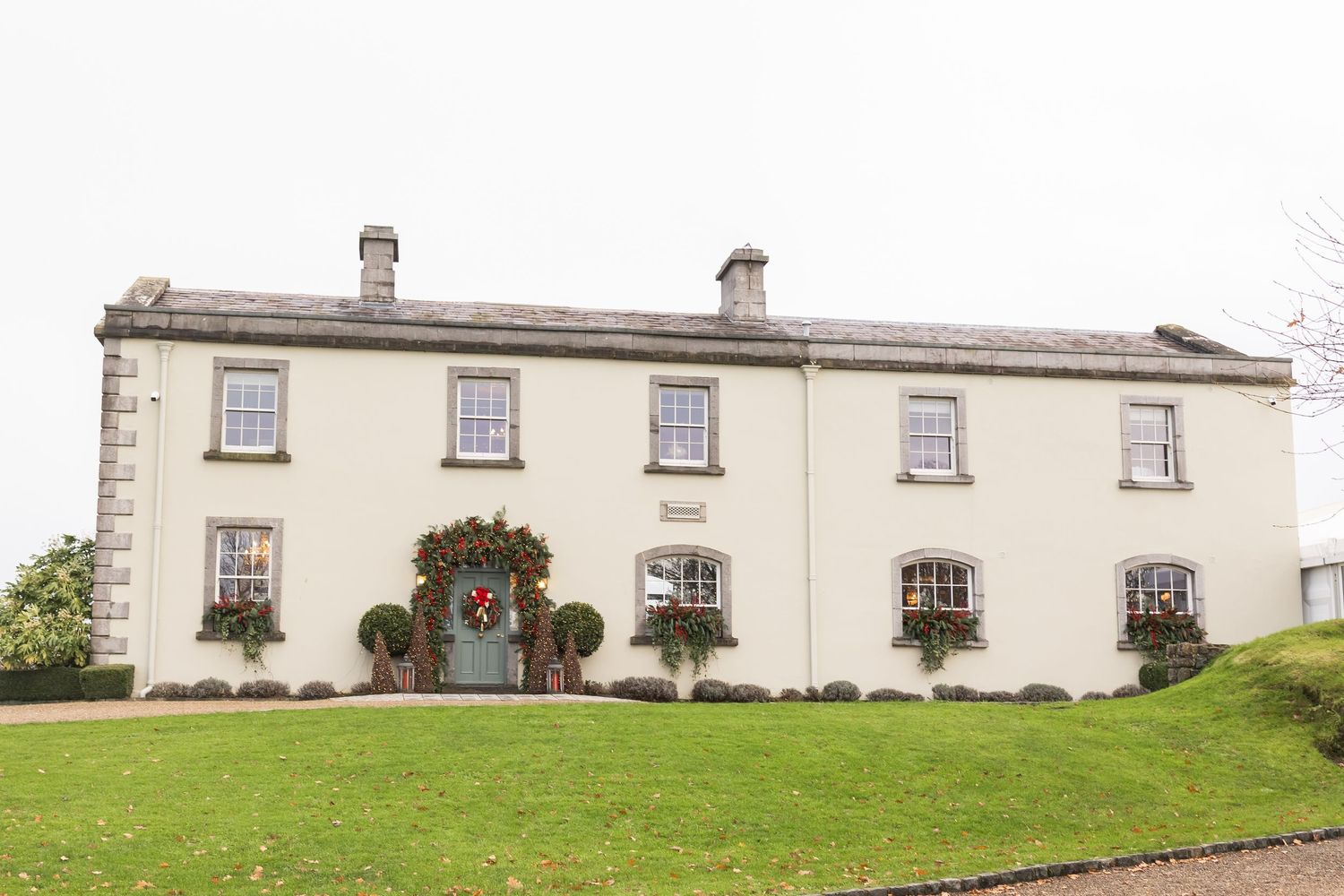 A charming two-story white country house with festive Christmas wreaths on windows and door.