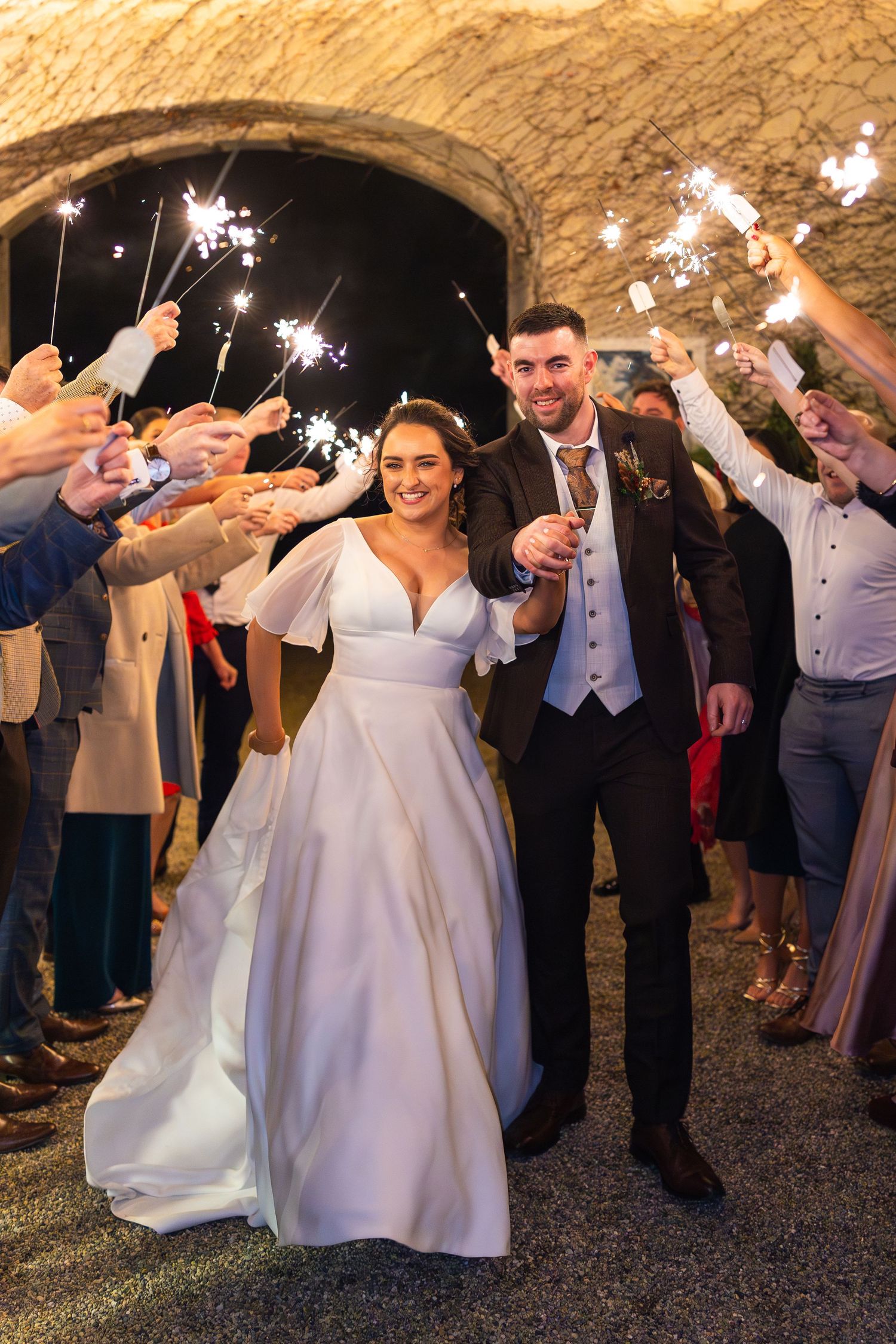 Wedding celebration at night with guests holding sparklers creating a magical illuminated walkway.