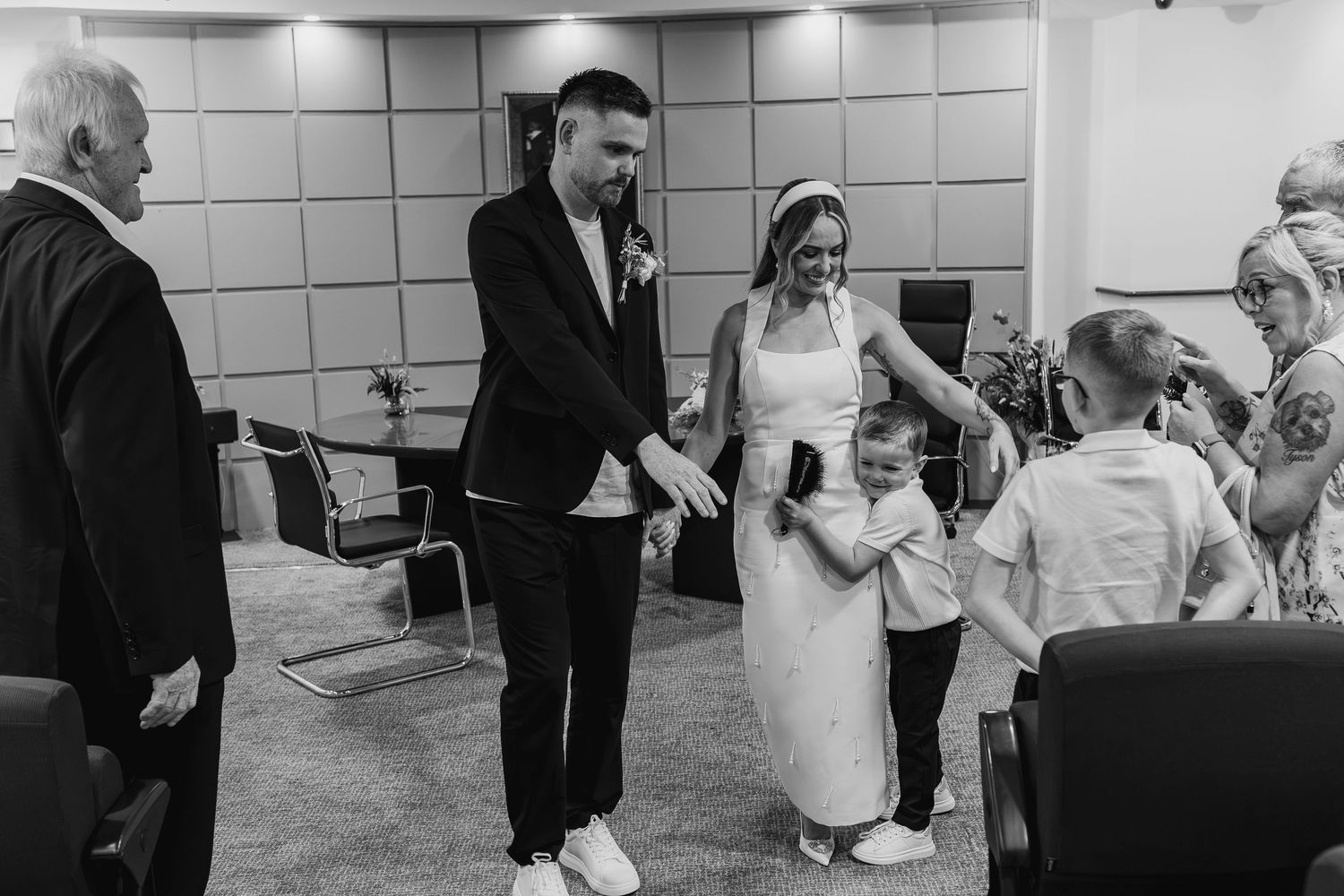 Black and white wedding photo of bride and groom greeting young child guest in a registry office ceremony.