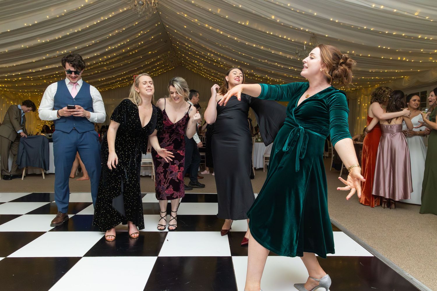 Wedding guests dancing energetically on black and white checkered dance floor at reception.