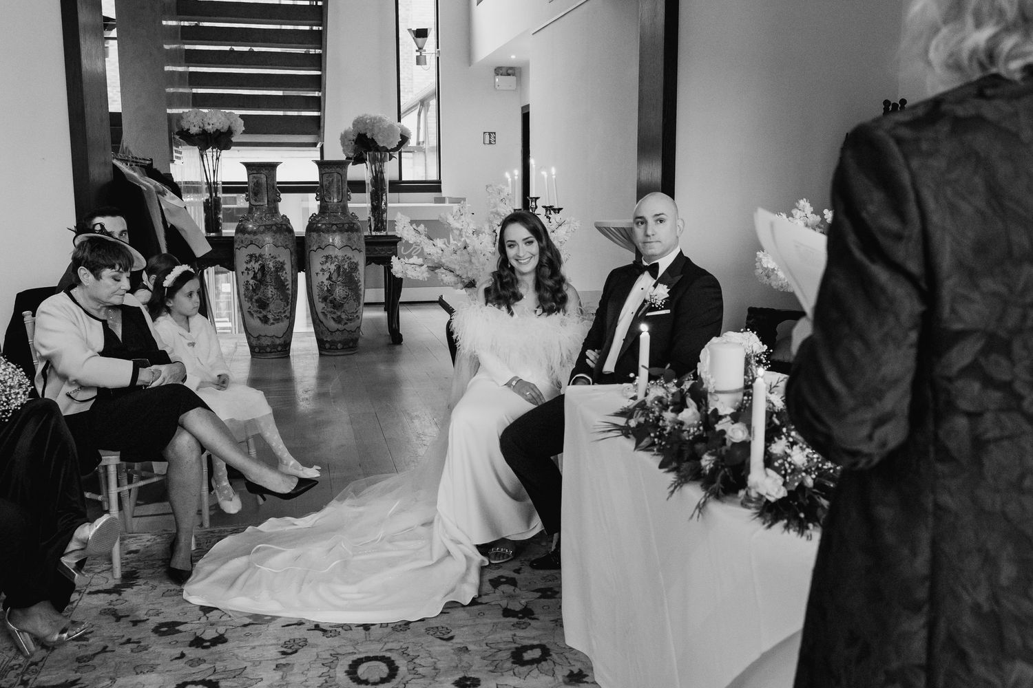 Wedding guests gather around a beautifully decorated reception table with elegant floral centerpieces.