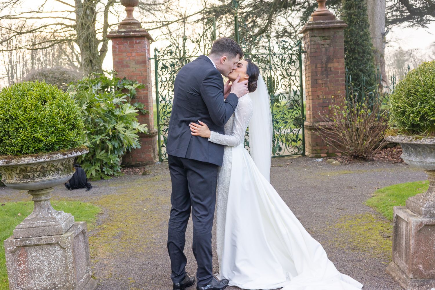Romantic wedding portraits captured along a garden path with decorative stone pillars and greenery.