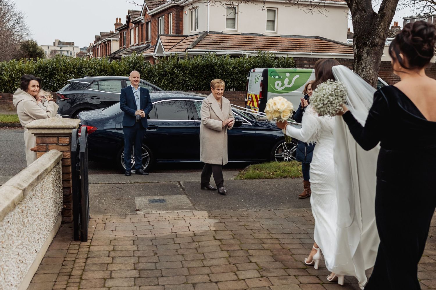 Wedding guests and party members walking outside a brick building on a cloudy day.