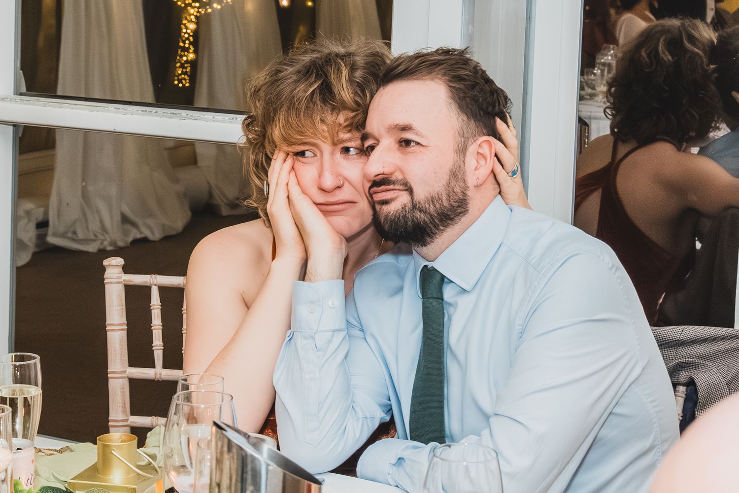 Couple sharing tender moment at wedding reception, woman resting head on mans shoulder at decorated table.