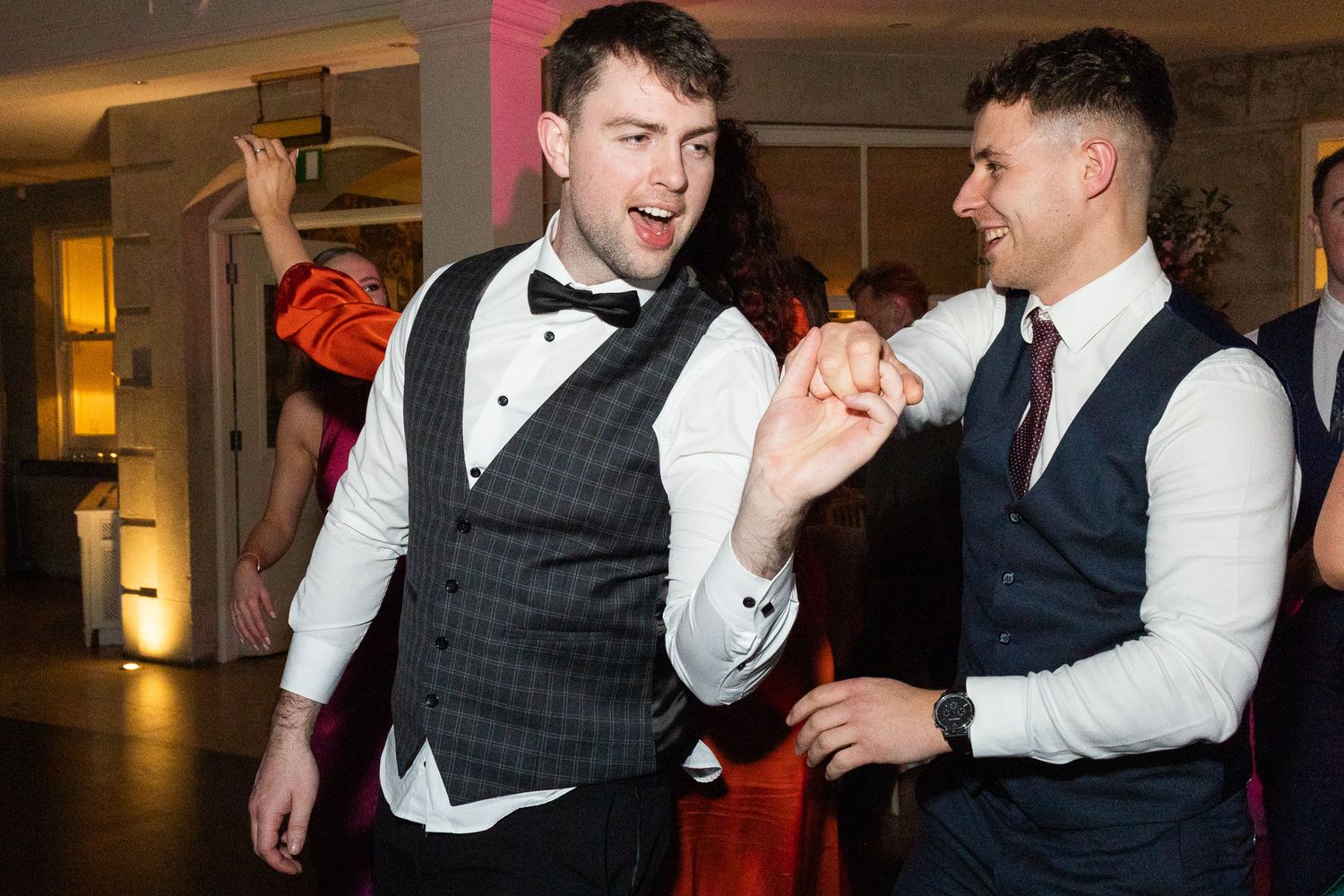 Two guests in formal vests enjoying a lively dance at Dublin wedding celebration.