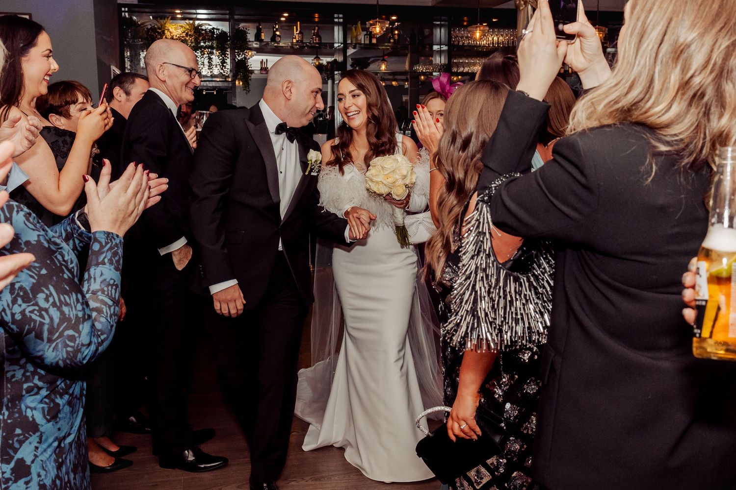 Wedding guests dance and celebrate on a dimly lit dance floor at a reception party.