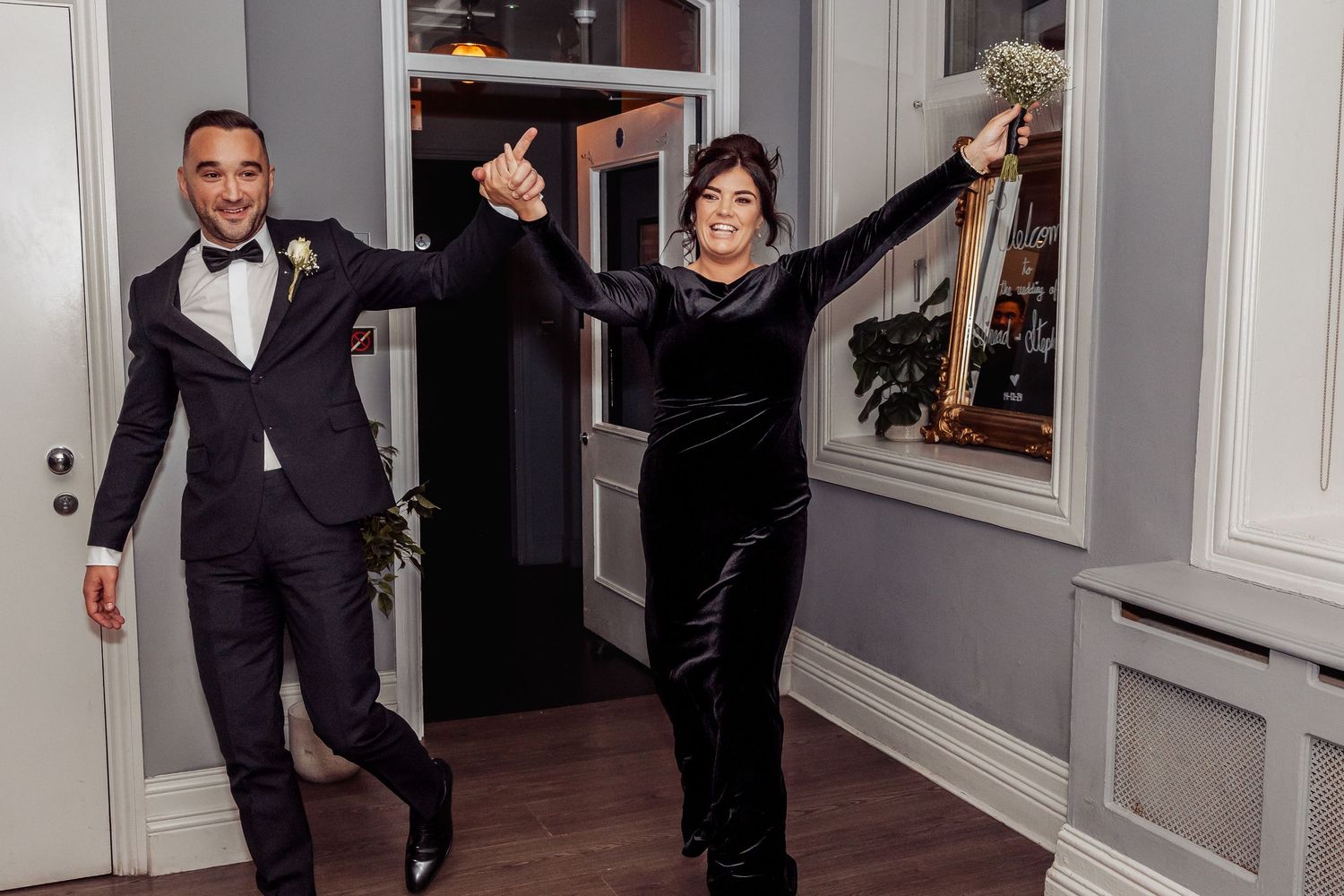Groomsmen in tuxedos posing playfully in hallway during wedding celebrations.