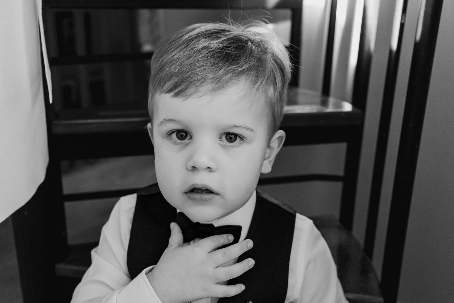 Black and white portrait of a young boy in a vest and bow tie looking at the camera.
