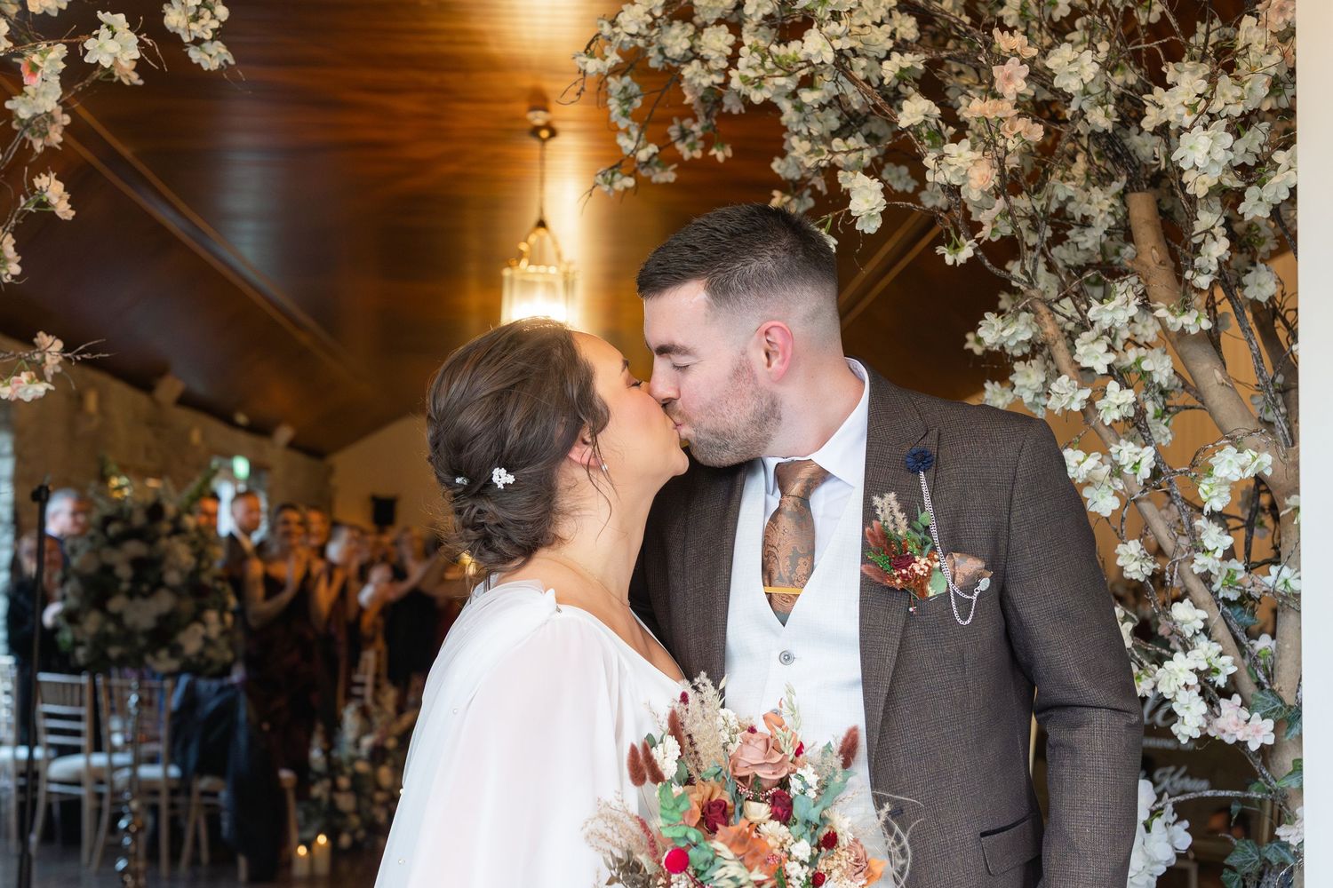 Bride and groom sharing a first kiss at the altar surrounded by white floral arch decorations.