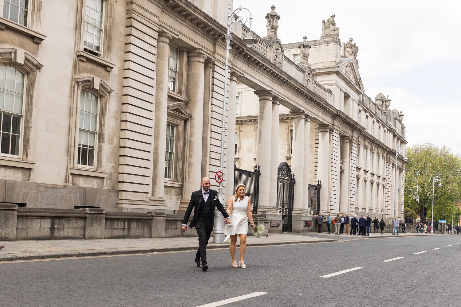 A couple runs joyfully along a grand historic building with classical architecture in an urban setting.