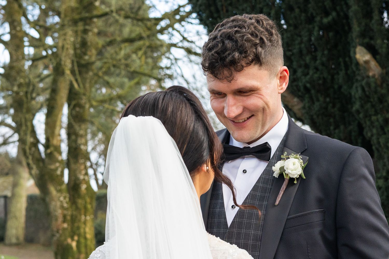 Wedding couple sharing unposed moments among tall trees in a garden setting.
