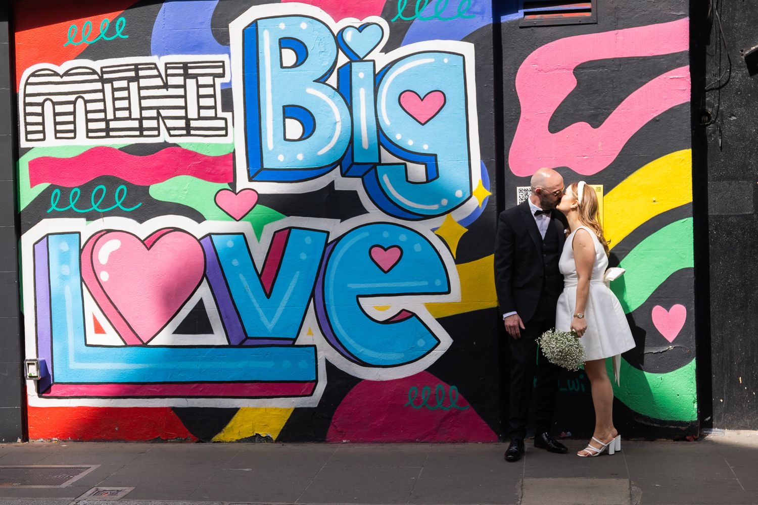 A couple poses against a colorful Dublin street art mural featuring the words 'Big Love' in vibrant letters.