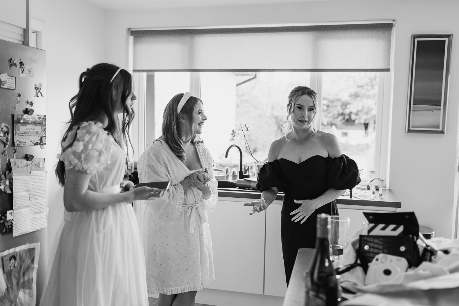 Three people gather in a bright kitchen during wedding preparations.