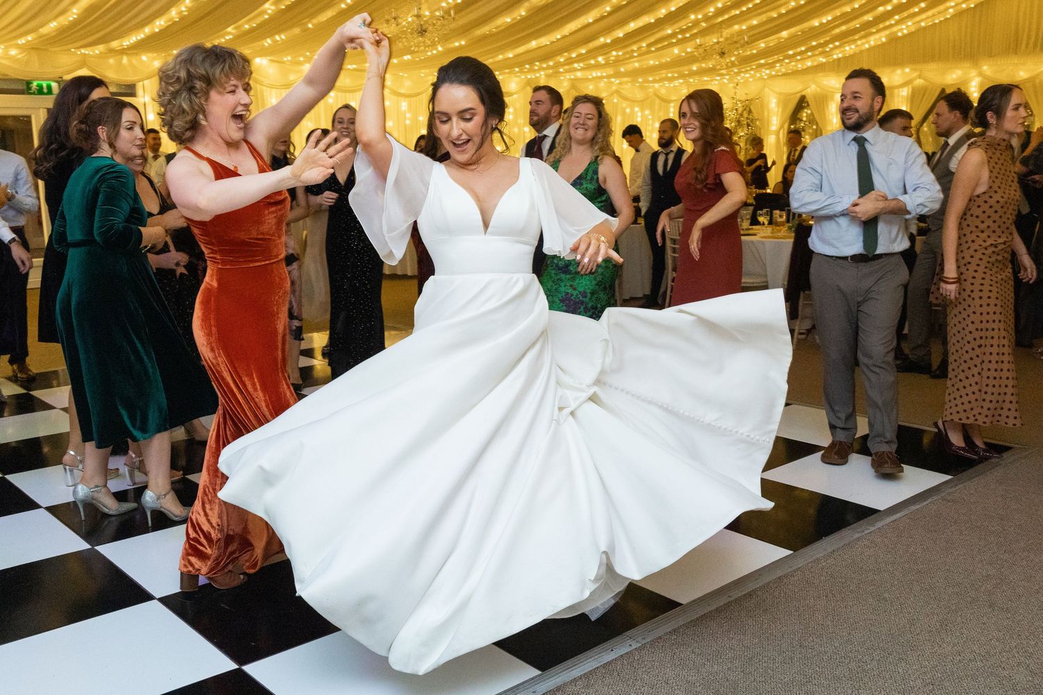 Wedding reception celebration with dancing and twirling in a golden-lit tent.