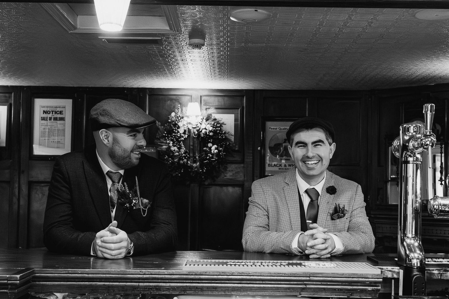 Black and white photo of people sitting at a dimly lit bar counter.