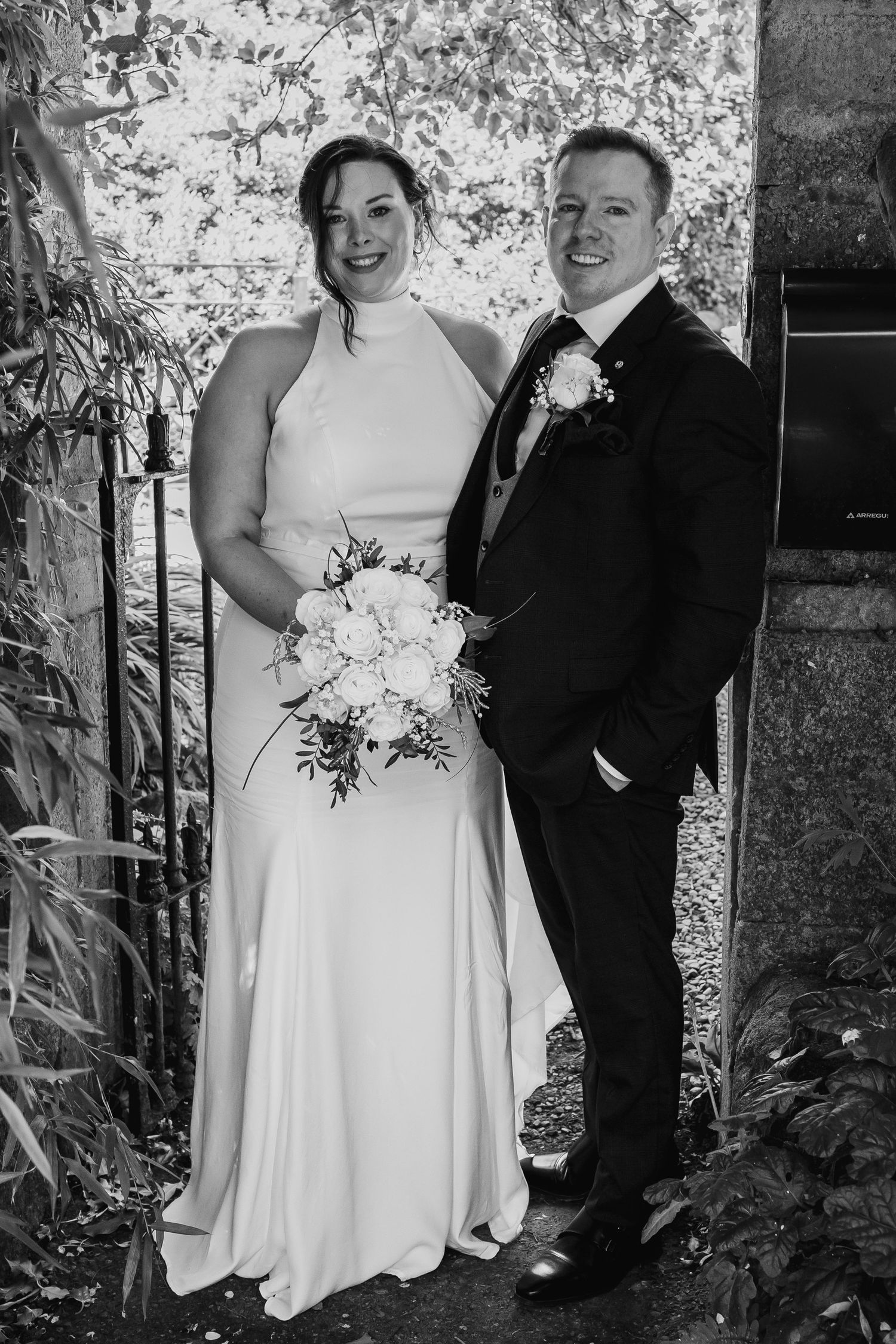 Black and white wedding photo of a smiling bride holding bouquet and groom in suit with boutonniere.