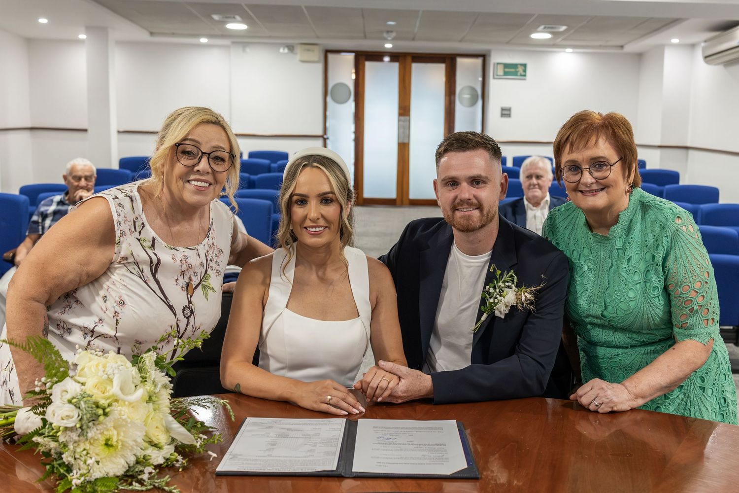 Couple signs wedding register with two female guests at a civil ceremony in a formal registry office setting.
