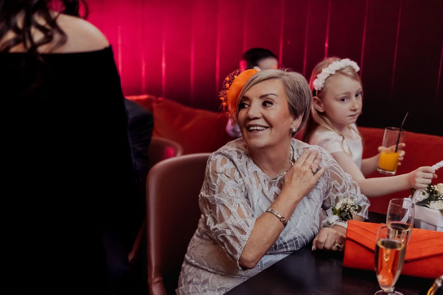 Wedding reception guests seated in red velvet booths enjoying drinks and conversation.