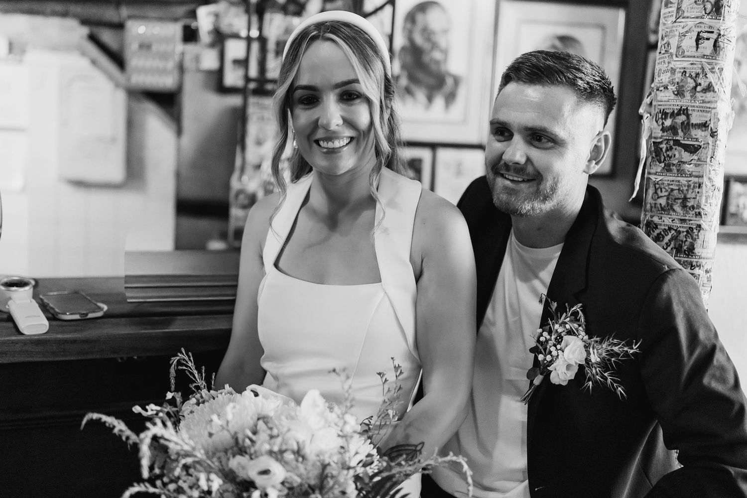 A smiling bride and groom pose together inside a pub in this black and white wedding photo.