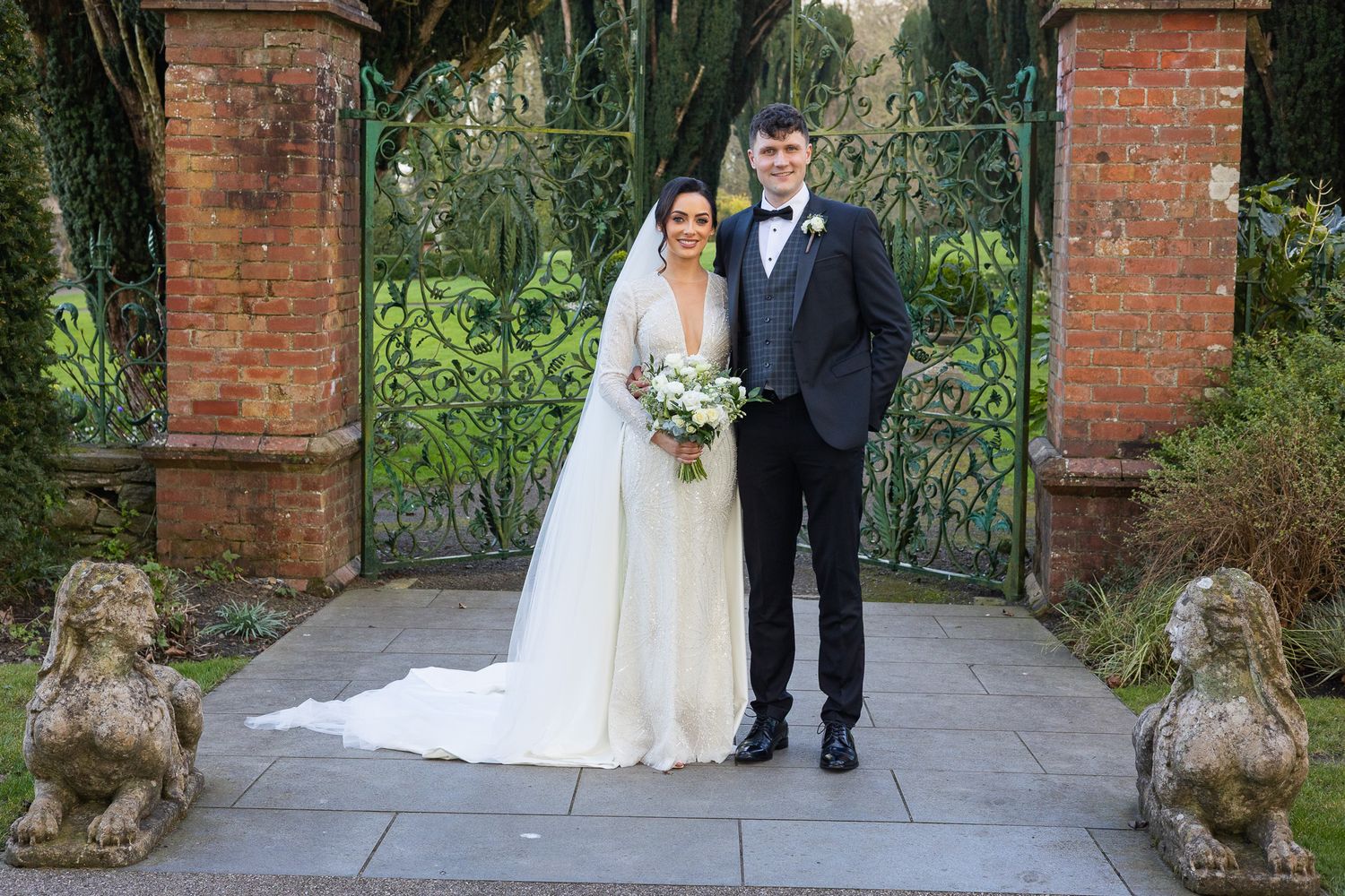 Elegant wedding portraits taken by Dublin wedding photographer by brick entrance gates with stone lion statues.