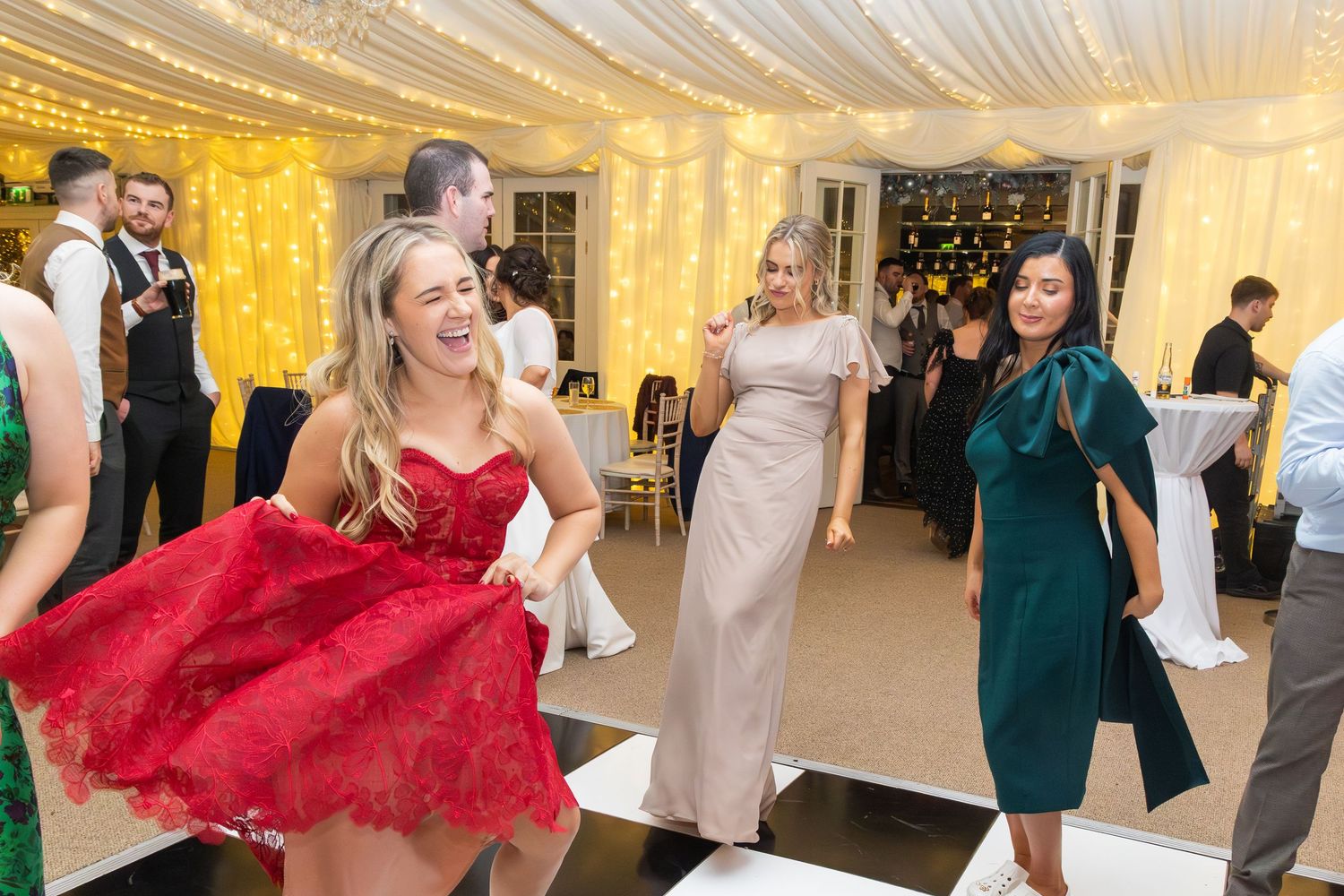 Guests dance joyfully at wedding reception in fairy light decorated marquee venue.