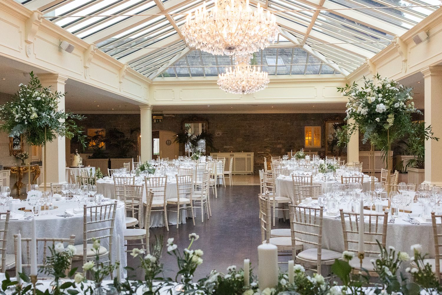 Tankardstown elegant wedding reception hall with crystal chandeliers and white table settings under a glass ceiling.