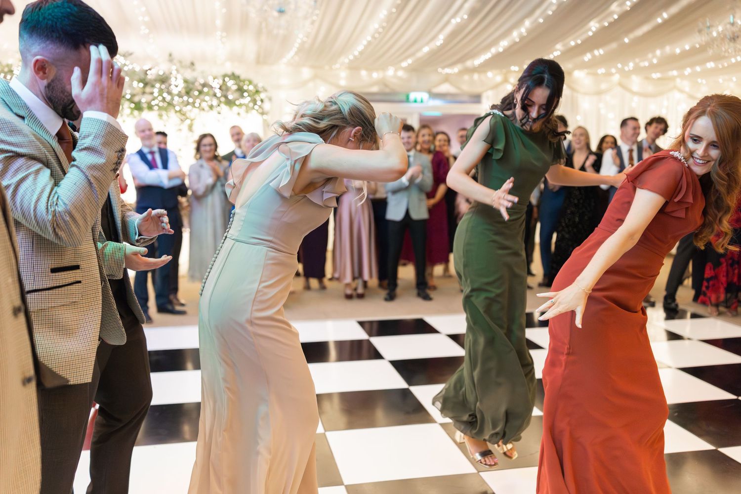 Guests dancing energetically on a black and white checkered dance floor at an elegant wedding reception.