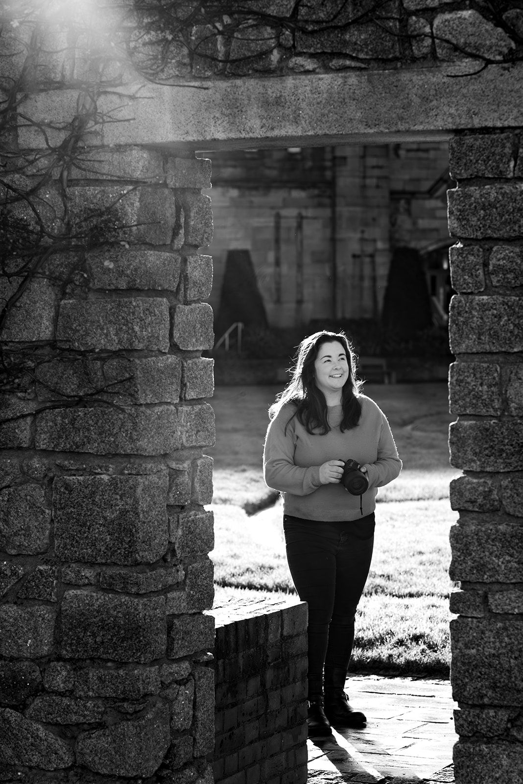 Artistic black and white portrait series through stone archway with natural backlighting.