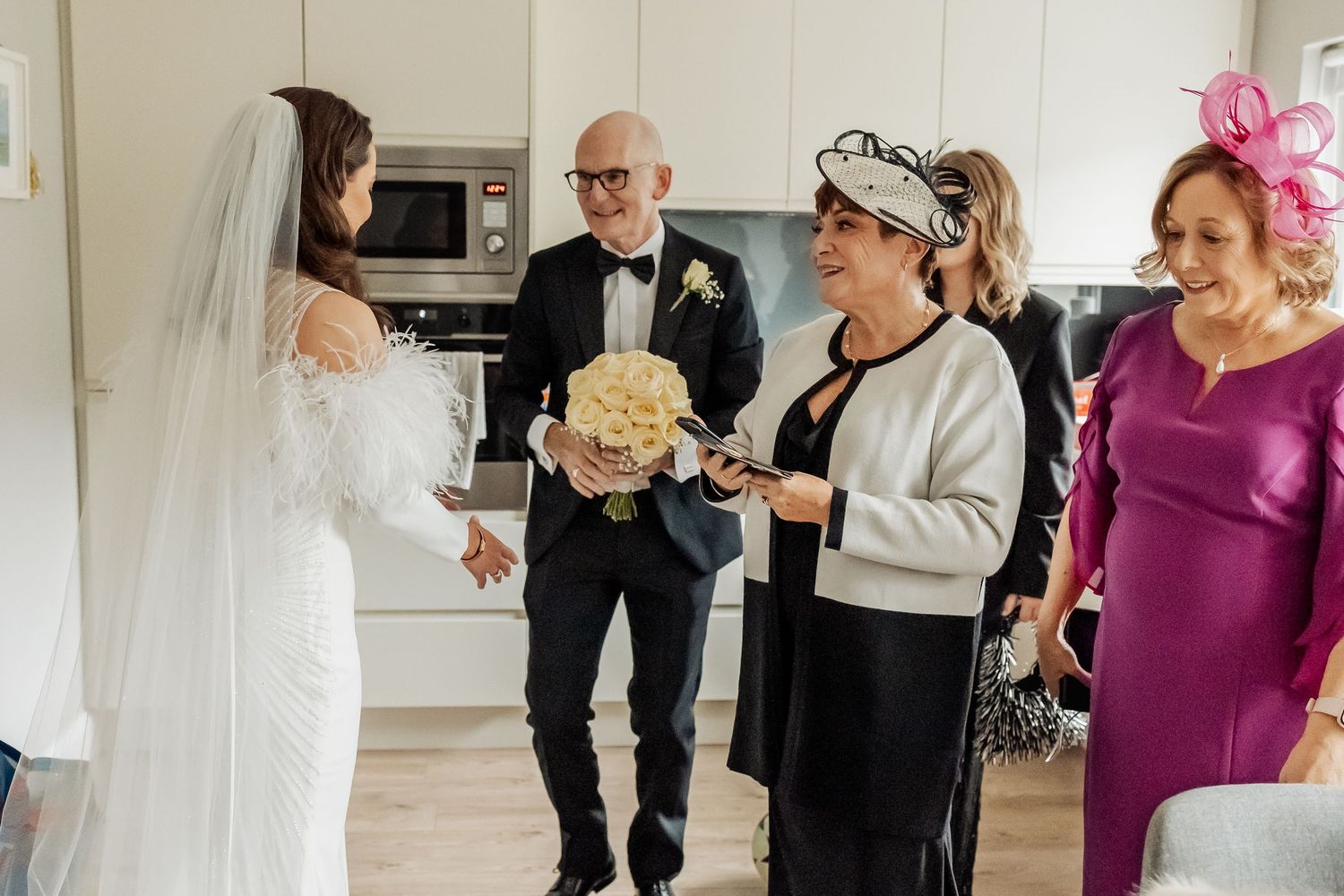 Wedding party members in formal attire gathered in a bright indoor space.
